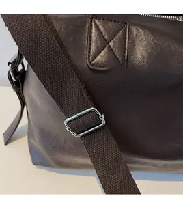 Detail of dark brown leather travel bag featuring adjustable fabric shoulder strap and silver buckle