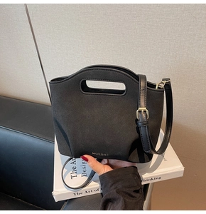 Detail of black bucket bag with cutout handle and gold hardware on white books