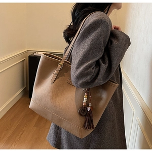 Detailed view of a tan pebble leather tote bag with decorative fringe and beaded charms