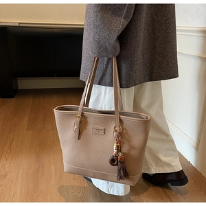 Detail view of beige lychee leather tote bag with ethnic tassel charm and fashion label