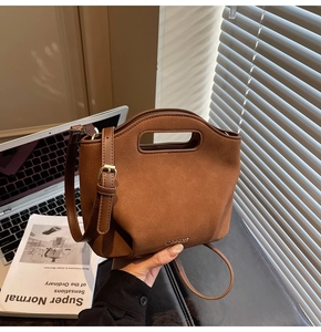 Detailed texture of dark brown suede bucket bag with metallic logo and cutout handle