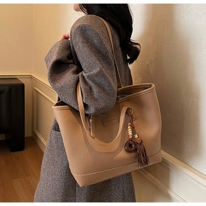 Detailed side view of light brown pebbled leather tote bag with stylish tassel pendant