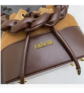 Detail of the braided leather handle and golden logo on the two-tone bucket bag