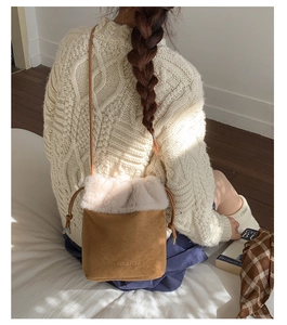 Close-up of brown suede bucket bag featuring white faux fur trim and branded detail