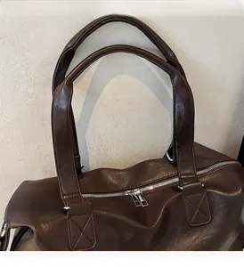 Detail of reinforced X-shaped stitching on handles and silver zipper of a brown travel bag