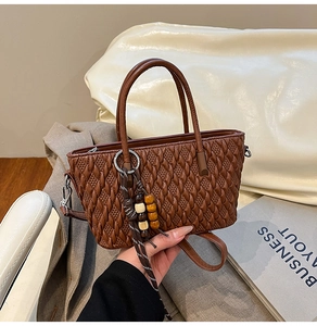 Detailaufnahme der braunen Plissee-Beuteltasche mit Holzperlenquaste und Rundgriff