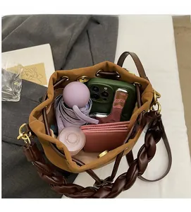 Top-down macro view of brown suede bucket bag interior with items and woven strap