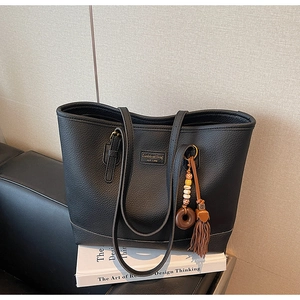 Detail of black pebbled leather tote bag with tassel pendant on stacked books