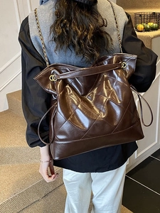 Deep brown quilted leather tote bag with gold chain strap worn by a model in interior