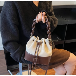 Detail view of two-tone bucket bag with braided handle and AEKD logo in leather
