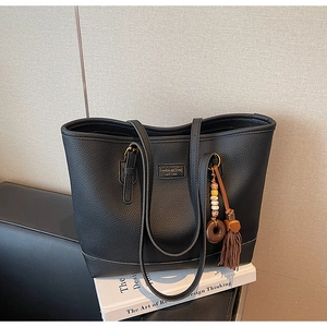 Detail of black pebbled PU leather tote bag with boho tassel charm and New York label