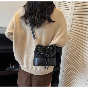 Detail of black bucket bag with woven handle and contrast leather stitching on model