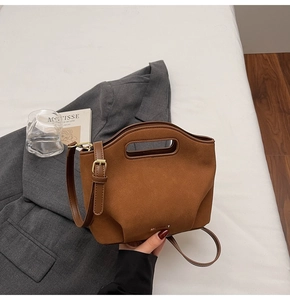 Close-up of caramel brown matte leather bucket bag with cutout handle on white bedding
