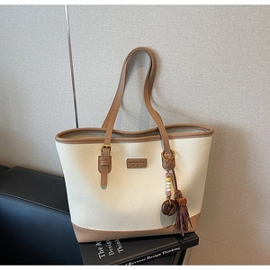 Detail of beige tote bag with brown leather handles and decorative tassel ornament