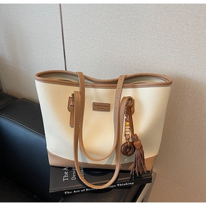 Macro detail of creamy white lychee grain leather tote bag with brown trim and tassel charm