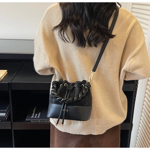 Detail view of black leather bucket bag with braided handle and gold drawstring hardware