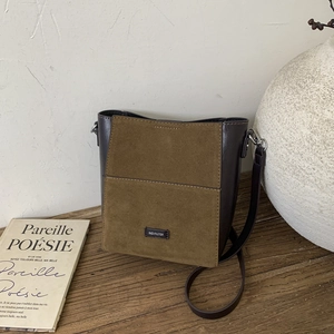 Close-up of vintage bucket bag with green suede and brown leather on a wooden table