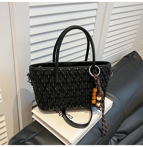 Detail der schwarzen Beuteltasche mit Flechtstruktur und Anhänger aus Holzperlen