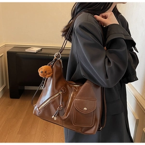 Detail of dark brown tote bag showing side view with bear pendant and metal rings