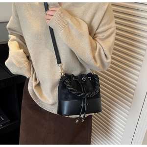 Detail of black drawstring bucket bag featuring woven handle and gold logo hardware