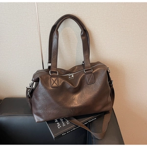 Detail of dark brown leather travel tote with reinforced stitching and dual silver zippers