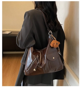Deep brown shoulder bag with decorative zippers and a cute plush bear pendant accessory