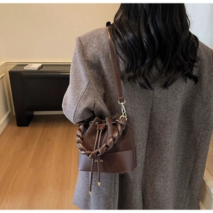 Detail of dark brown bucket bag with braided handle worn over a grey blazer