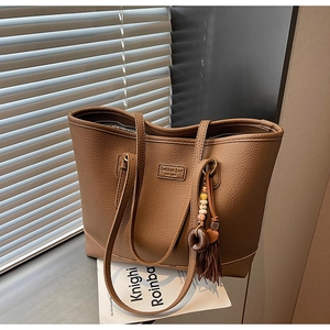 Macro view of brown lychee-patterned leather tote bag with boho tassel and logo detail