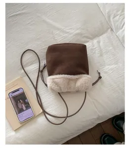 Brown suede bucket bag with white faux fur trim and embroidery on white bedding