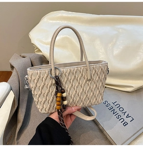 Detail der beigen gesteppten Beuteltasche mit Webstruktur und Holzperlen-Anhänger