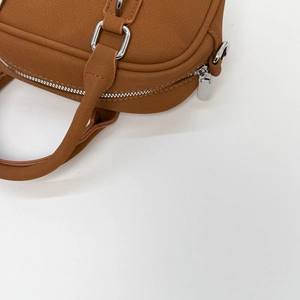 Close-up of caramel brown matte leather bag with silver metal zipper and buckle detail