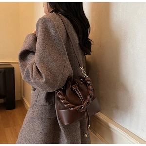 Detail of dark brown bucket bag with braided handle and mixed suede leather texture