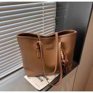 Detail of brown leather tote bag with tassel charm and textured finish on a windowsill