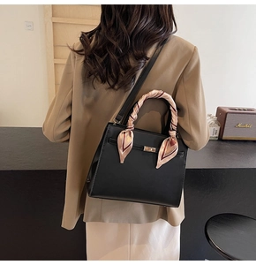Détail du sac à main en cuir noir avec fermoir doré et foulard en soie sur la poignée