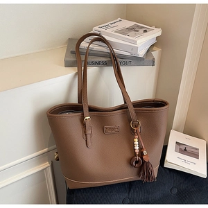 Detail of brown litchi pattern tote bag with tassel pendant and fashion bag label
