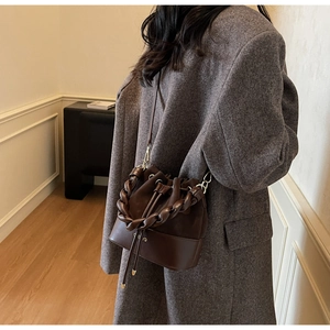 Detail view of brown suede bucket bag with chain strap styled on a wool coat