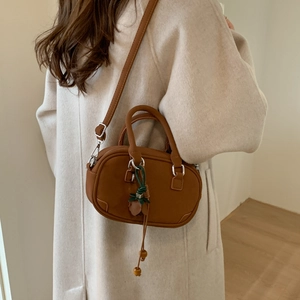 Brown leather crossbody bag detail with green tassel charm on a wool coat model