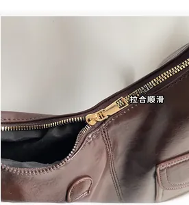 Detail view of the smooth golden metal zipper closure on a coffee brown faux leather bag