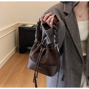 Close-up of dark brown bucket bag featuring a braided handle and gold drawstring details