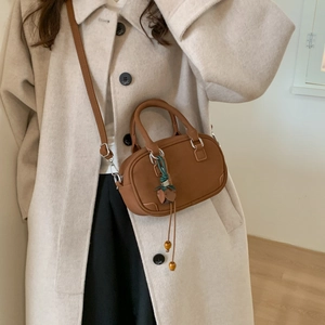 Detail of caramel leather crossbody bag with green leaf charm on a neutral coat