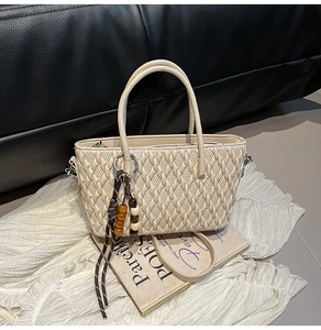 Detail der gewebten Textur cremeweißen Beuteltasche mit Metallring und Perlenquaste