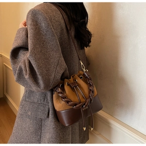 Close-up of brown bucket bag with braided handle and drawstring on grey wool blazer
