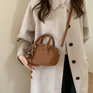 Detail of brown vintage crossbody bag with long tassel charms worn on beige coat