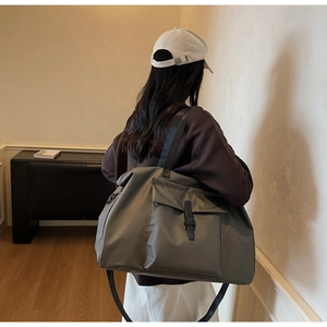 Rear view of a model carrying a large grey travel bag with buckle front pocket detail