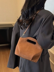 Brown suede bucket bag with hollow handle and shoulder strap worn over a grey blazer