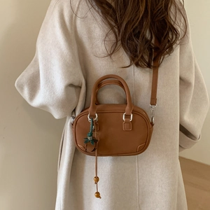 Detailed view of caramel leather handbag with leaf charm and adjustable shoulder strap