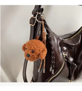 Brown curly plush poodle charm keychain attached to a premium dark brown leather tote bag