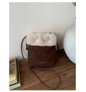 Detail view of brown suede bucket bag with white faux fur trim on a wooden surface