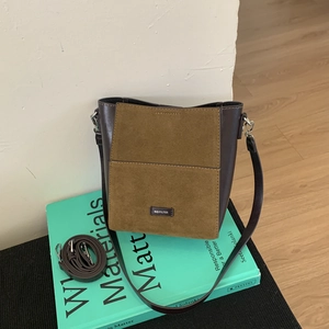 Detail of a bucket bag featuring dark leather and olive green suede with logo tag