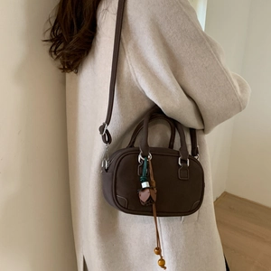 Detail of a dark brown cylinder bag with suede texture and wooden tassel charm